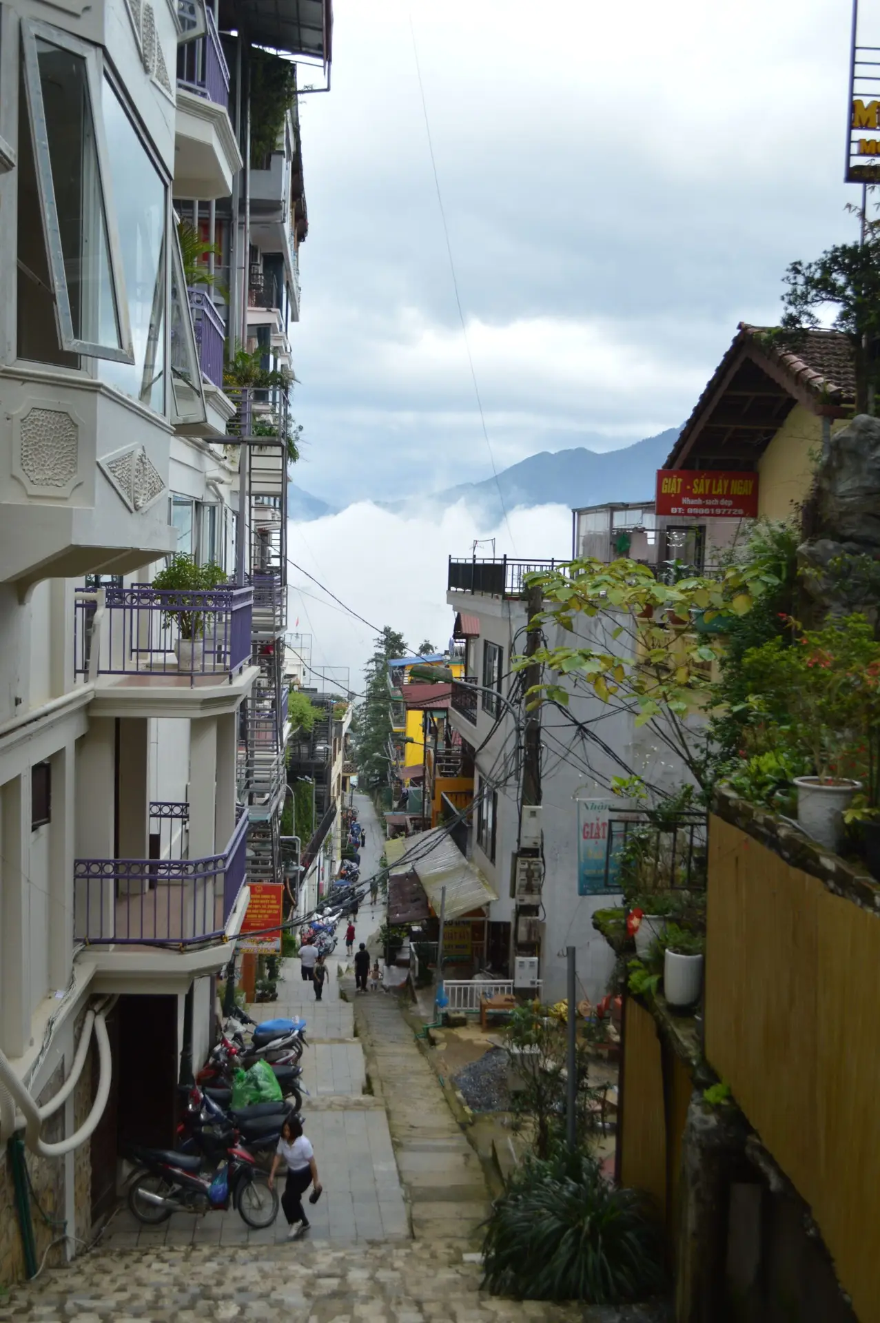 Charming street with colorful houses in Sapa, Vietnam, offering a scenic view of mountains and clouds.